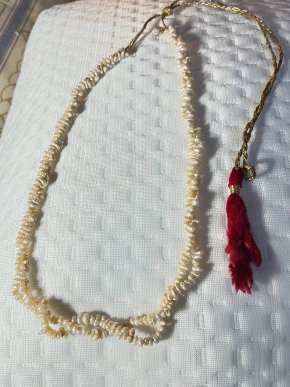 Mwhite seed or rice pearl necklace accented with a red tassel